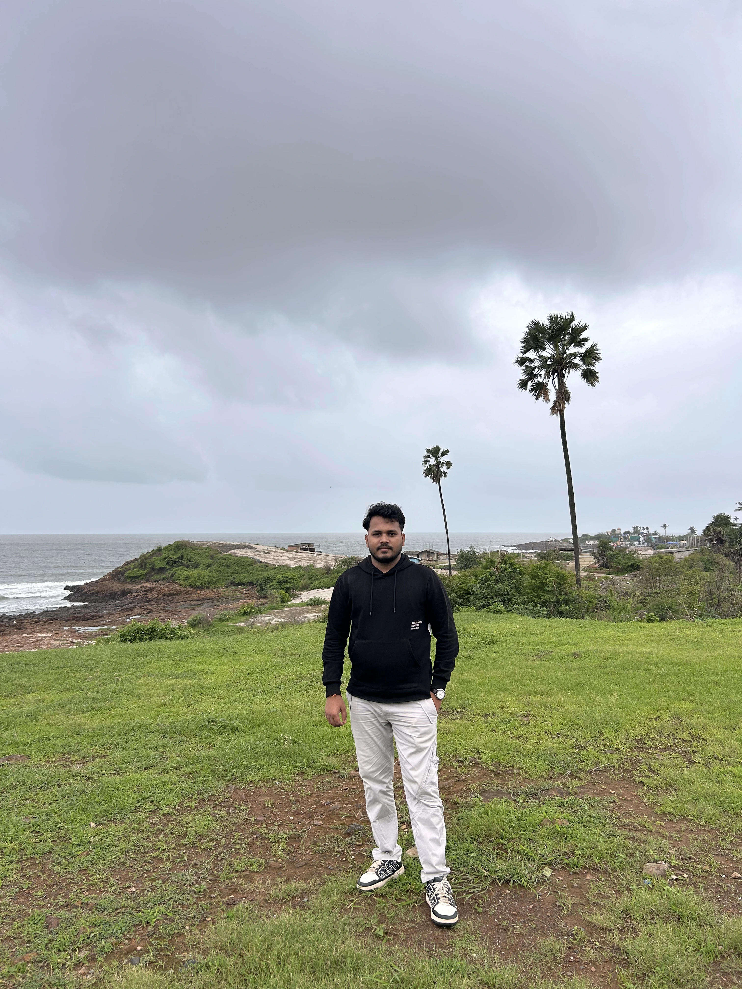 Rohit Meher standing on a green hillside by the sea